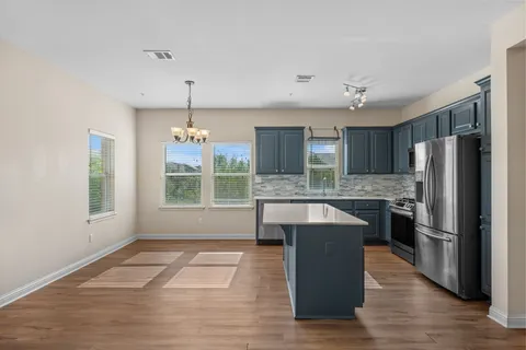 a kitchen with stainless steel appliances granite countertop a refrigerator a sink dishwasher a stove and a dining table with wooden floor