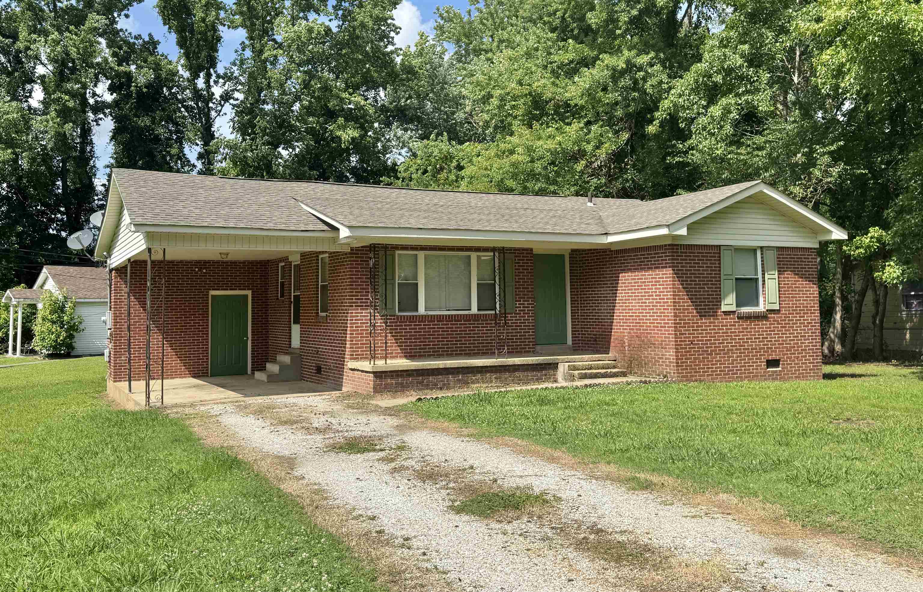 Ranch-style house featuring dirt driveway, a front lawn, brick siding, an attached carport, and roof with shingles