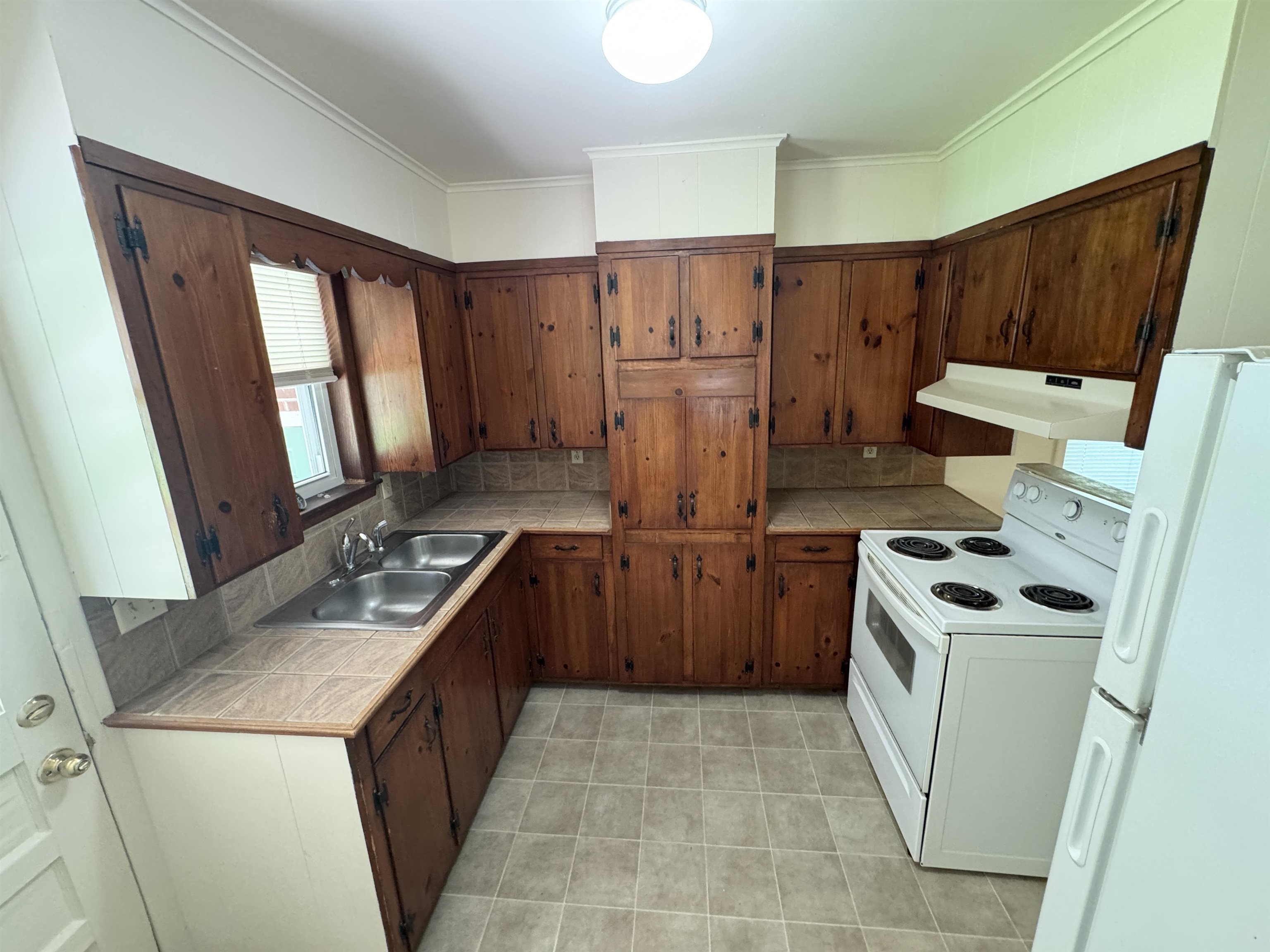 Kitchen featuring white range with electric cooktop, under cabinet range hood, fridge, tile counters, and light tile patterned floors