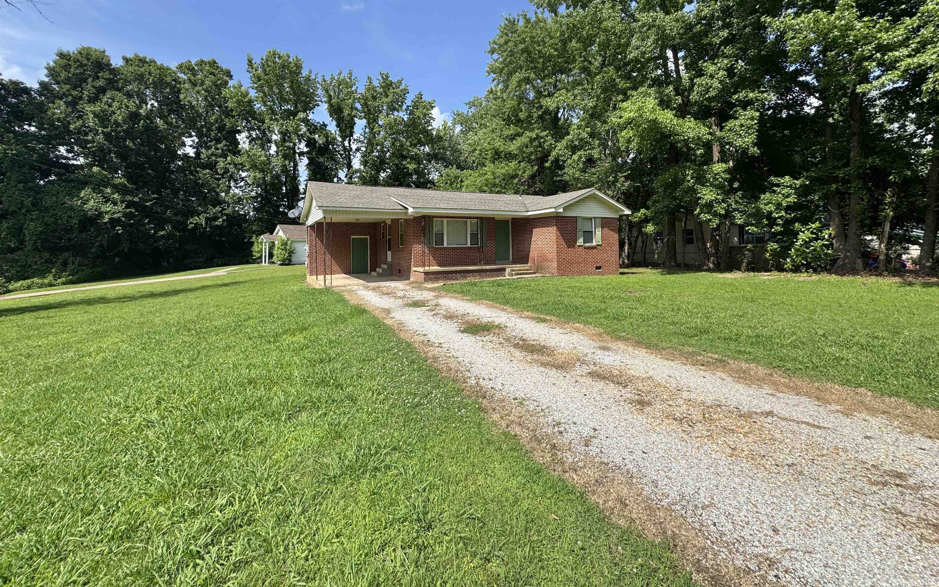 119 Larkwood Avenue Ripley, TN 38063 - Photo 10 of 10 Ranch-style house featuring gravel driveway, a front yard, brick siding, an attached carport, and view of wooded area