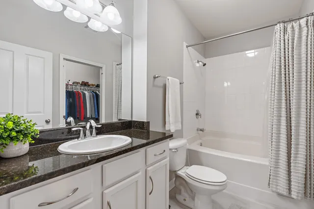 a bathroom with a granite countertop sink a toilet a mirror a vanity a bathtub and shower