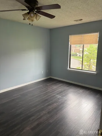 an empty room with wooden floor fan and windows