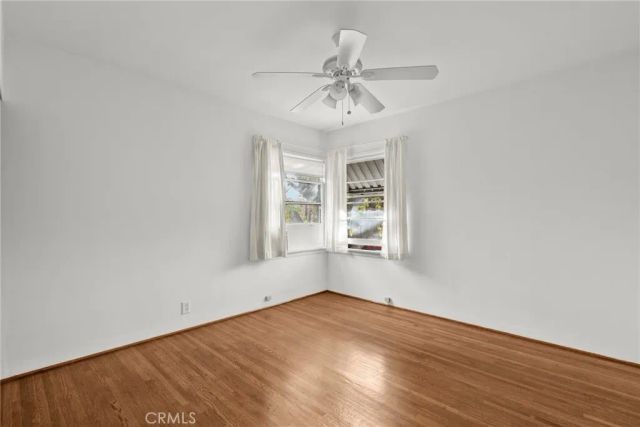 an empty room with wooden floor chandelier fan and windows