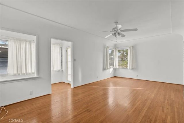 an empty room with wooden floor chandelier fan and windows