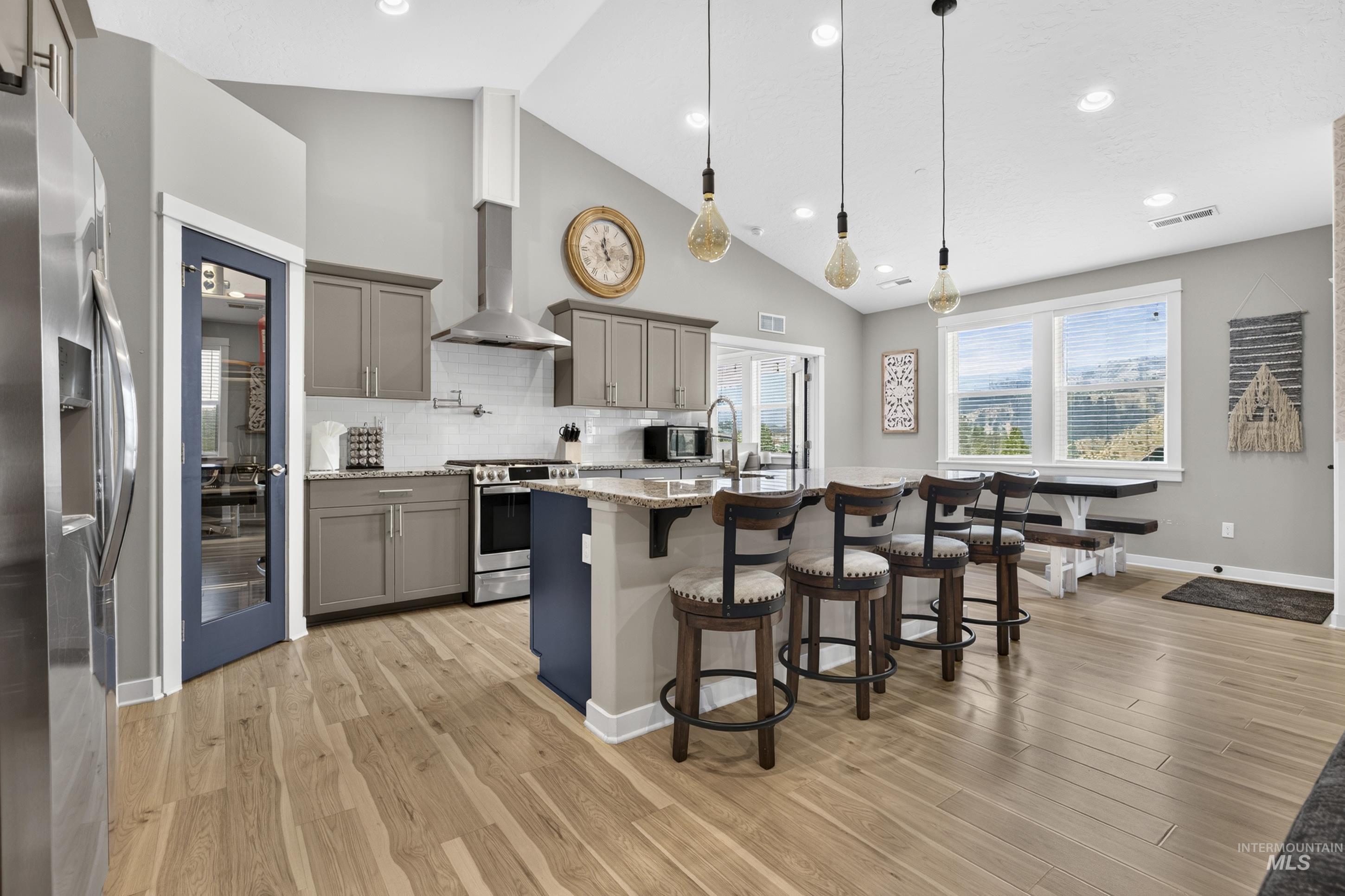 132 Mores Creek Rim Road Boise, ID 83716 - Photo 9 of 44 Vaulted ceilings, wood-finish flooring, island with countertop seating, stainless steel appliances, and large windows