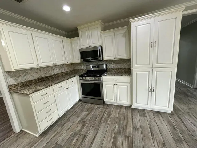 a kitchen with stainless steel appliances granite countertop a stove a sink and white cabinets
