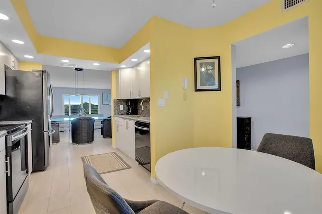 a kitchen with stainless steel appliances kitchen island granite countertop a refrigerator a oven a sink a dining table and chairs with wooden floor