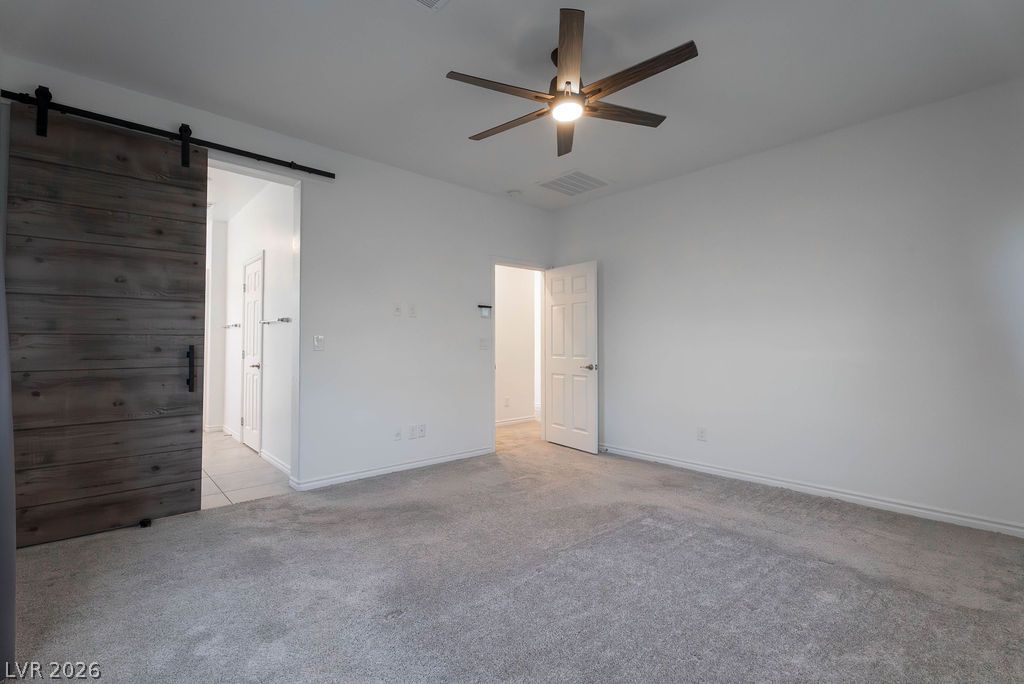 7126 Calvert Cliffs Street North Las Vegas, NV 89084 - Photo 22 of 44 An inviting sleeping space with a modern barn door and ceiling fan, offering a private retreat.