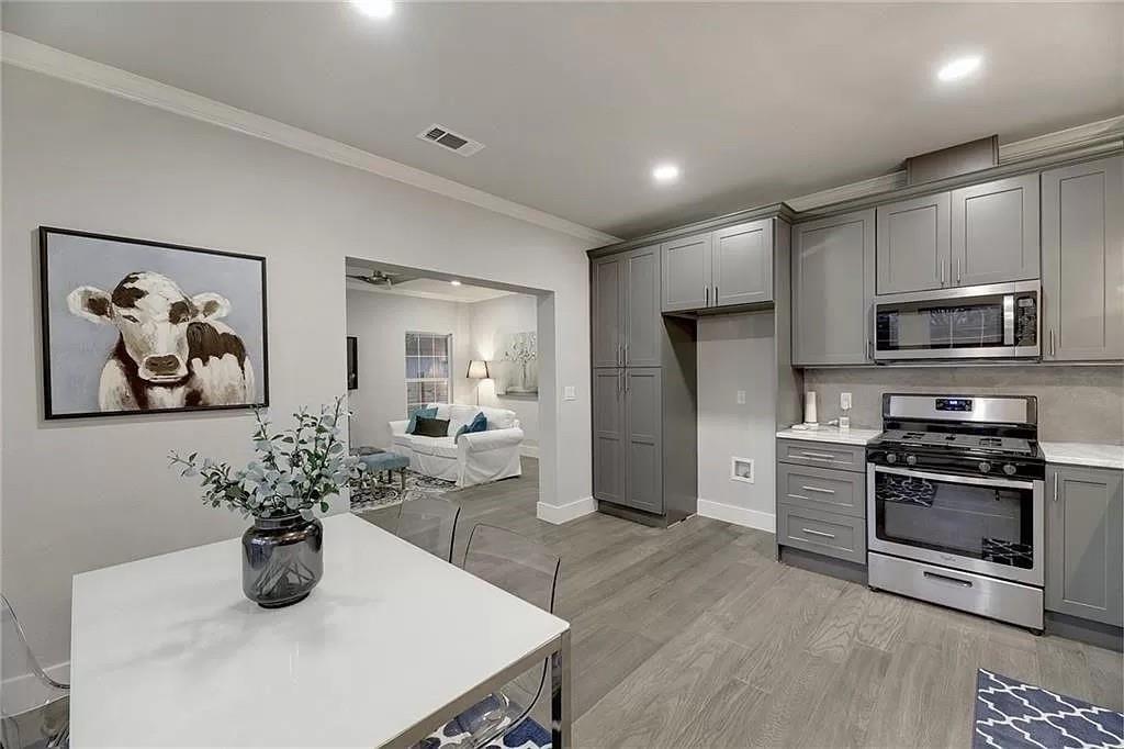 1217 Eleanor Street Austin, TX 78721 - Photo 8 of 17 Kitchen featuring gray cabinets, stainless steel appliances, light wood-style floors, ornamental molding, and light stone countertops
