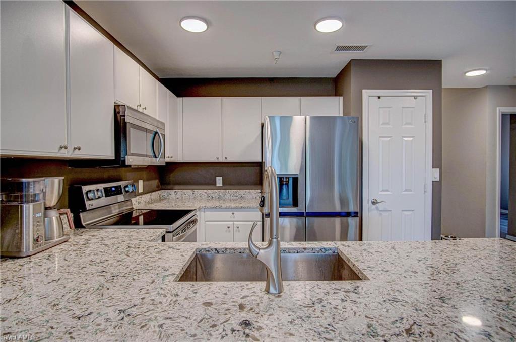 4450 Botanical Pl Circle, Unit 406 Naples, FL 34112 - Photo 3 of 16 a kitchen with stainless steel appliances granite countertop a refrigerator a stove and a sink with wooden floor