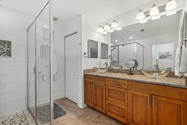 a bathroom with a granite countertop double vanity sink mirror and shower