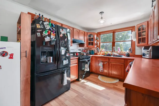 a kitchen with stainless steel appliances granite countertop a refrigerator a sink dishwasher a stove and a dining table with wooden floor