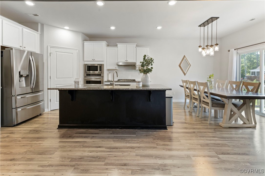 9801 Cravensford Loop Midlothian, VA 23112 - Photo 19 of 49 a kitchen with stainless steel appliances granite countertop a refrigerator a stove a sink a dining table and chairs with wooden floor