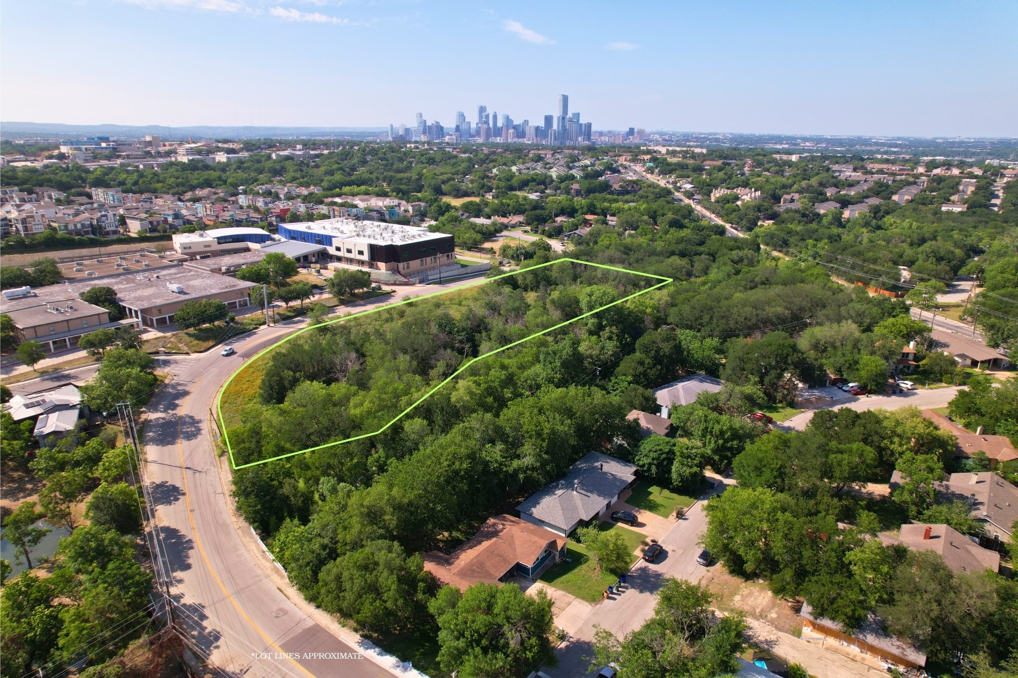 2813-2827 Metcalfe Road Austin, TX 78741 - Photo 1 of 13 An aerial panorama reveals a vast, tree-filled lot bordering a residential street with Austin city skyline views.