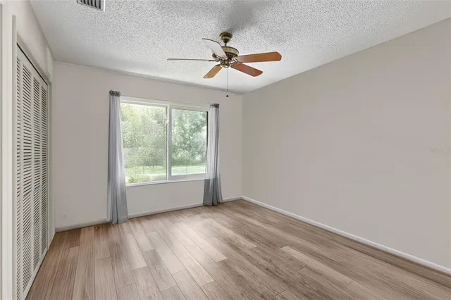 an empty room with wooden floor fan and windows