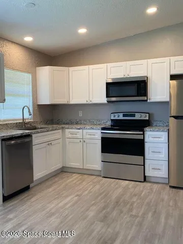 a white kitchen with granite countertop a stove top oven a sink and dishwasher a oven with white cabinets