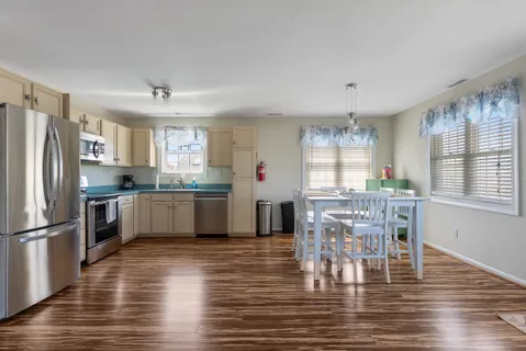 a kitchen with stainless steel appliances granite countertop a refrigerator a stove a sink dishwasher a dining table and chairs with wooden floor