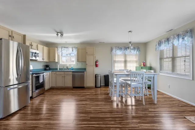a kitchen with stainless steel appliances granite countertop a refrigerator a stove a sink dishwasher a dining table and chairs with wooden floor