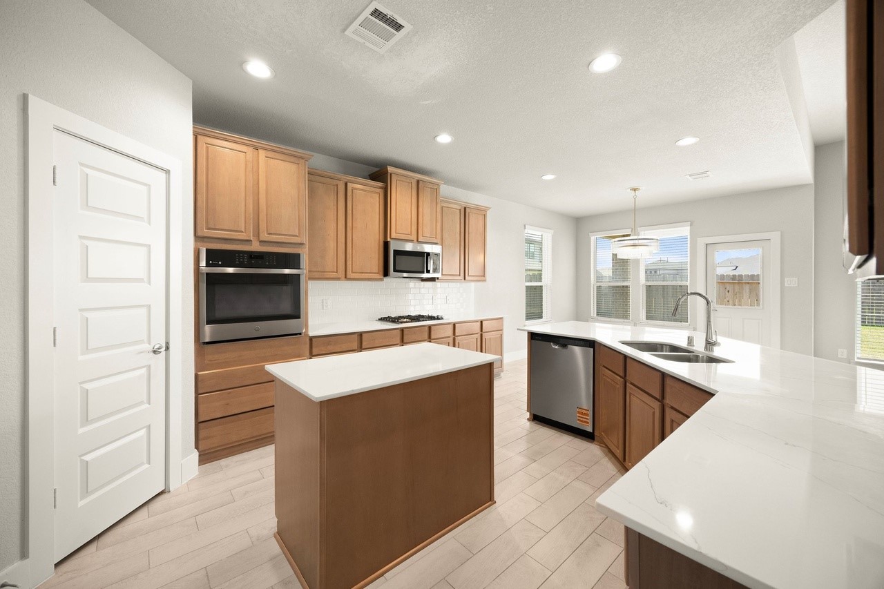 3018 North Spring Drive Spring, TX 77373 - Photo 12 of 25 Bright and spacious kitchen featuring modern appliances, ample wooden cabinetry, and a central island. Large windows provide plenty of natural light, complemented by sleek countertops and a stylish pendant light over the dining area.