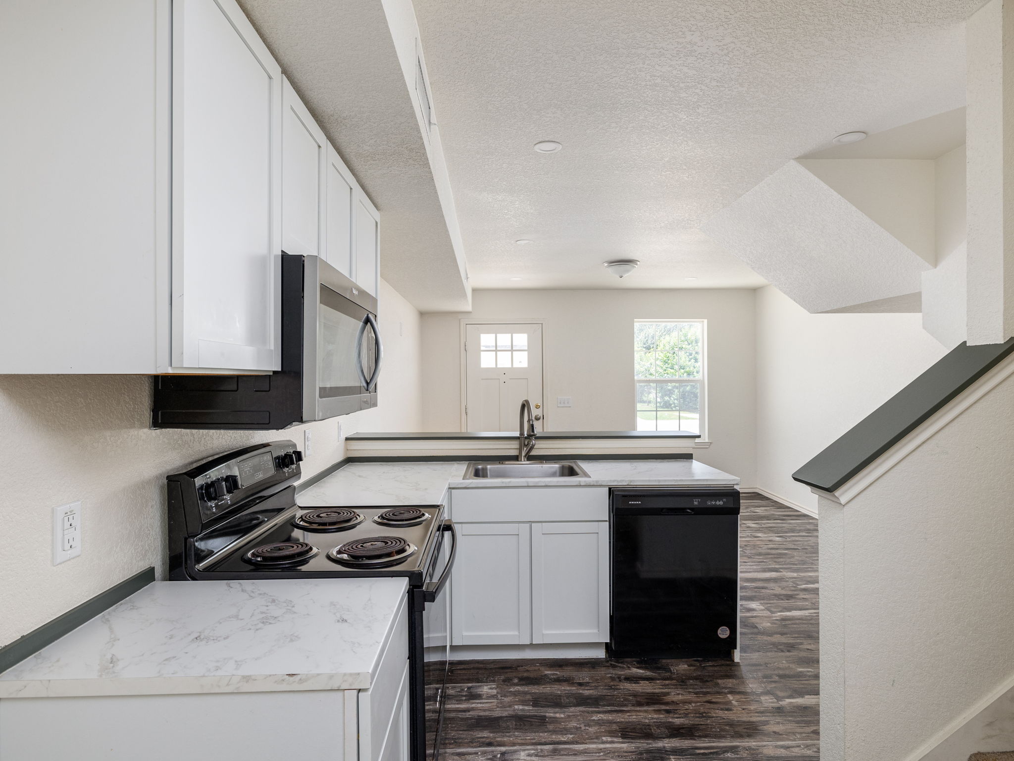 230 Debus Drive, Unit 108B Taylor, TX 76574 - Photo 8 of 16 Kitchen featuring black appliances, a peninsula, a textured ceiling, dark wood-style floors, and white cabinets