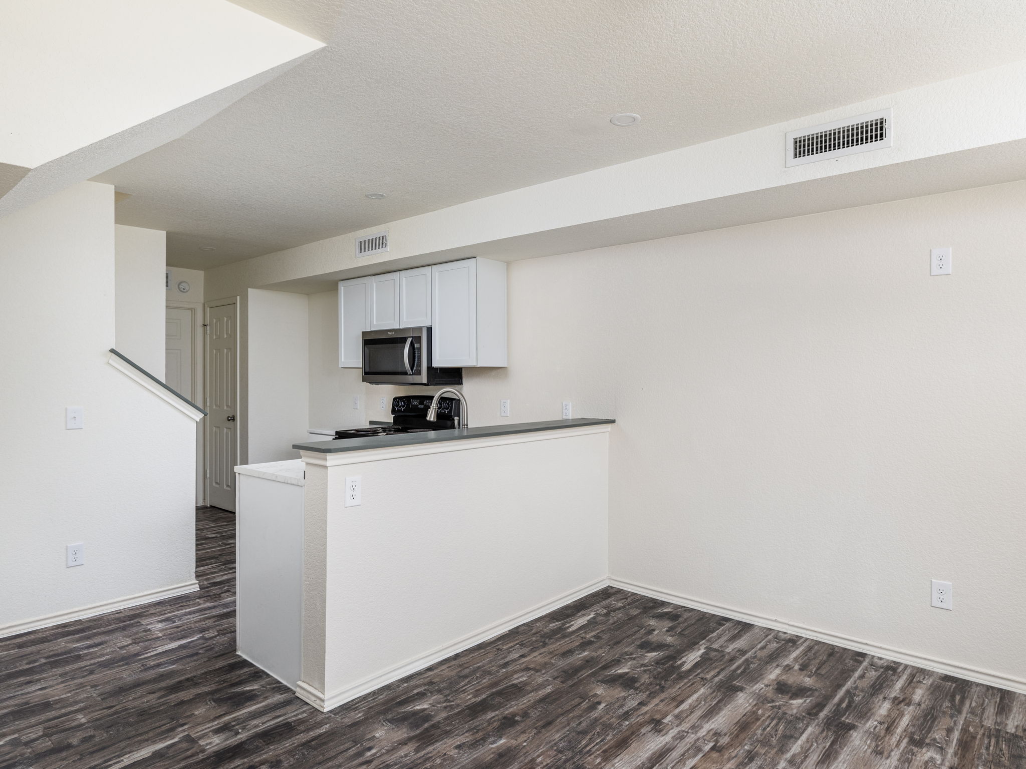 230 Debus Drive, Unit 108B Taylor, TX 76574 - Photo 9 of 16 Kitchen featuring white cabinets, dark wood-type flooring, a textured ceiling, a peninsula, and stainless steel microwave