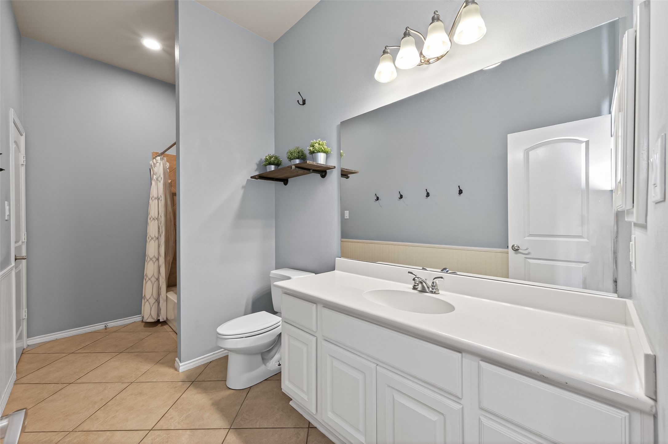 27443 Rebecca Field Lane Spring, TX 77386 - Photo 23 of 31 This bathroom features a spacious layout with a large vanity and ample countertop space. It includes a shower tiled flooring, and soft gray-blue walls. A large mirror and overhead lighting enhance the brightness of the room.