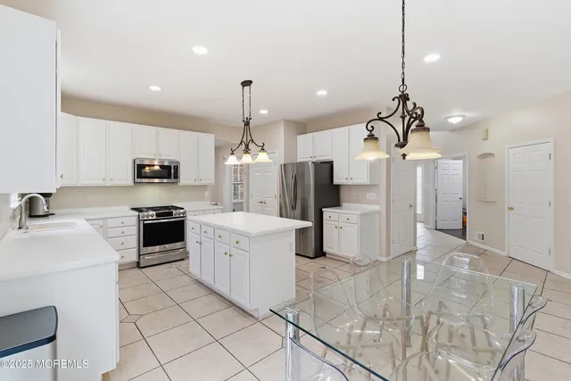 a kitchen with stainless steel appliances kitchen island granite countertop a refrigerator a sink dishwasher a stove and white cabinets with wooden floor
