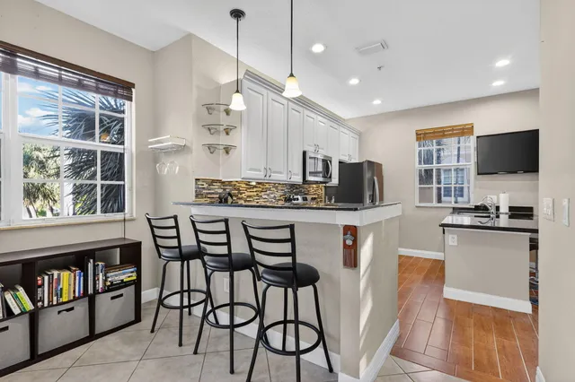 a kitchen with stainless steel appliances kitchen island granite countertop a dining table chairs and a refrigerator