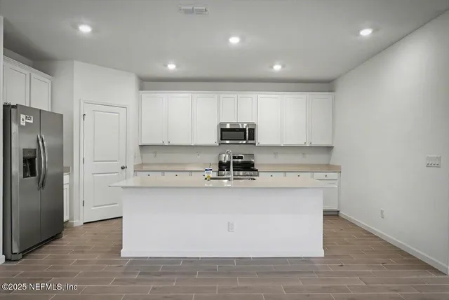 a kitchen with stainless steel appliances granite countertop a stove a sink a refrigerator and white cabinets with wooden floor