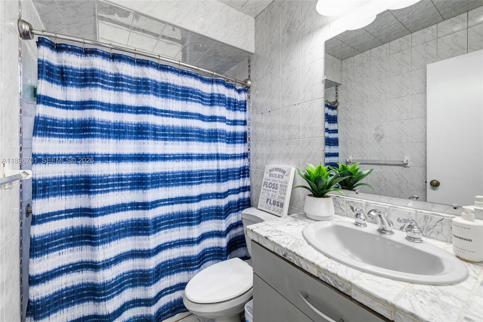 19491 Southwest 216th Street Miami, FL 33187 - Photo 19 of 32 a bathroom with a granite countertop sink a toilet a mirror and shower curtain
