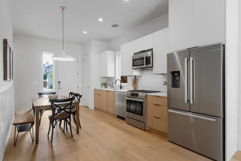 a kitchen with stainless steel appliances granite countertop a refrigerator a stove a sink a dining table and chairs with wooden floor