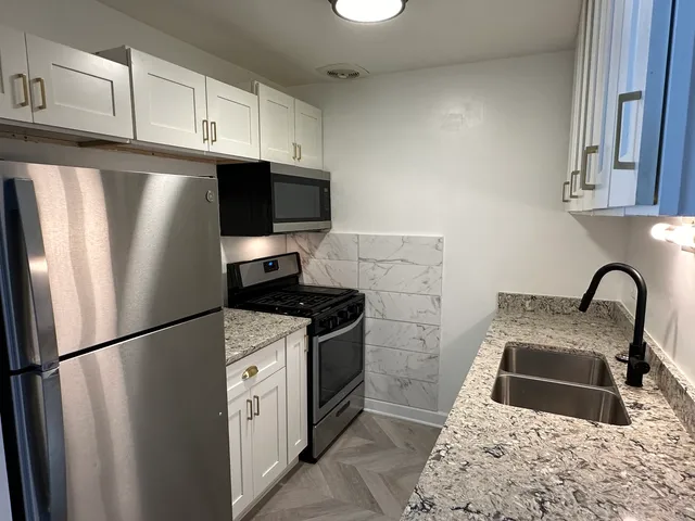 a kitchen with stainless steel appliances granite countertop a refrigerator a stove a sink and a white cabinets