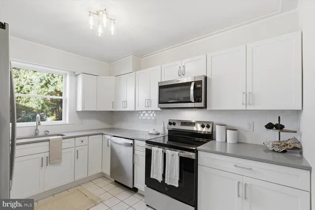 a kitchen with white cabinets appliances a sink and a window