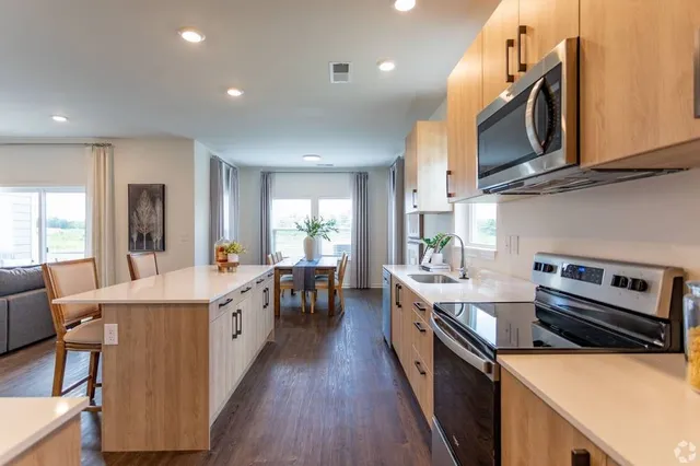 a kitchen with stainless steel appliances a stove a sink dishwasher a microwave oven and a dining table with wooden floor