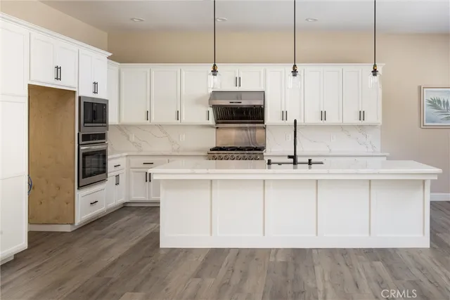 a kitchen with stainless steel appliances a stove a sink and white cabinets with wooden floors