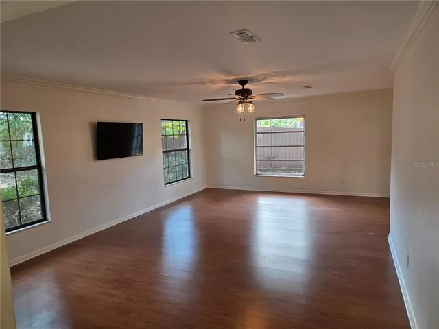 an empty room with wooden floor fan and windows