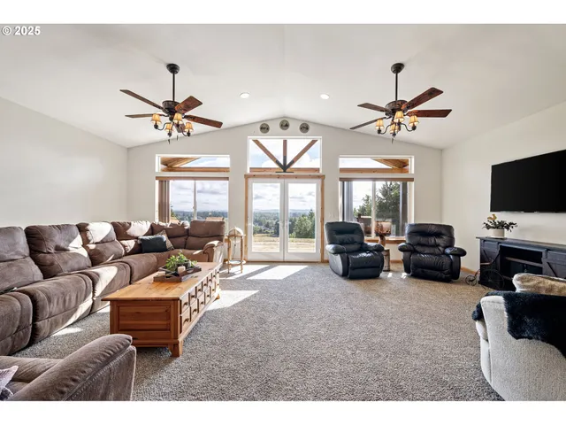a living room with furniture a ceiling fan a flat screen tv and a large window