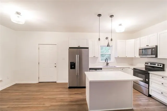 a kitchen with stainless steel appliances kitchen island granite countertop a sink a stove a refrigerator and island with wooden floor