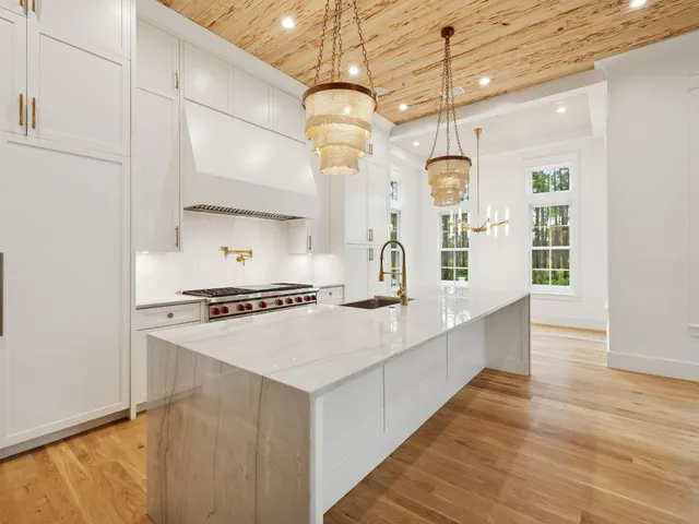 a large kitchen with stainless steel appliances a large counter top a stove a chimney and a chandelier