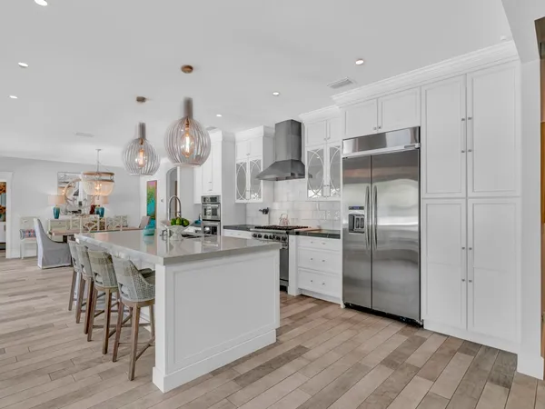 a kitchen with stainless steel appliances kitchen island granite countertop a refrigerator a stove a sink and white cabinets with wooden floor