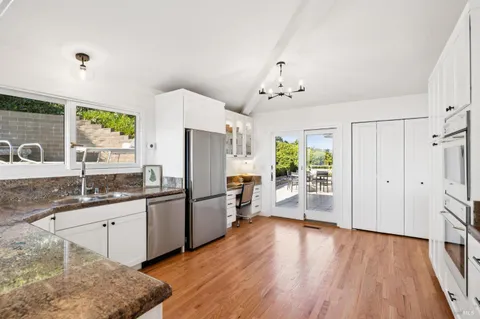 a kitchen with granite countertop a refrigerator a sink dishwasher a stove and white cabinets with wooden floor