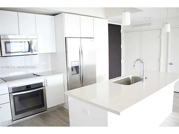 a kitchen with stainless steel appliances granite countertop a refrigerator a stove and white cabinets with wooden floor