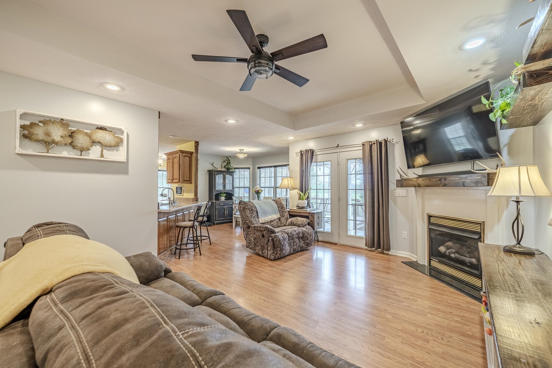 270 2 Boys Road Savannah, TN 38372 - Photo 7 of 35 Living room with a glass covered fireplace, light wood-type flooring, a tray ceiling, recessed lighting, and a ceiling fan
