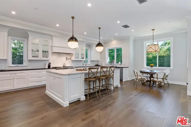 a kitchen with stainless steel appliances granite countertop a stove a sink dishwasher a refrigerator white cabinets with a dining table and chairs