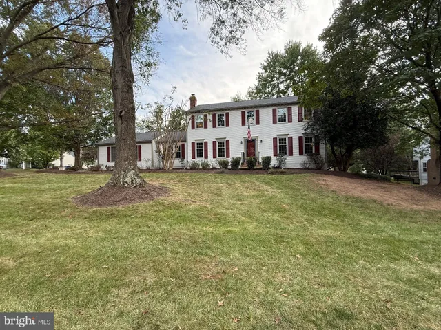 a view of a white house next to a yard with large trees