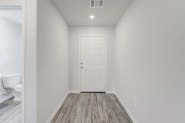 a view of a hallway with wooden floor and a toilet
