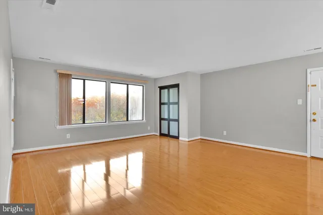 a view of an empty room with wooden floor and a window