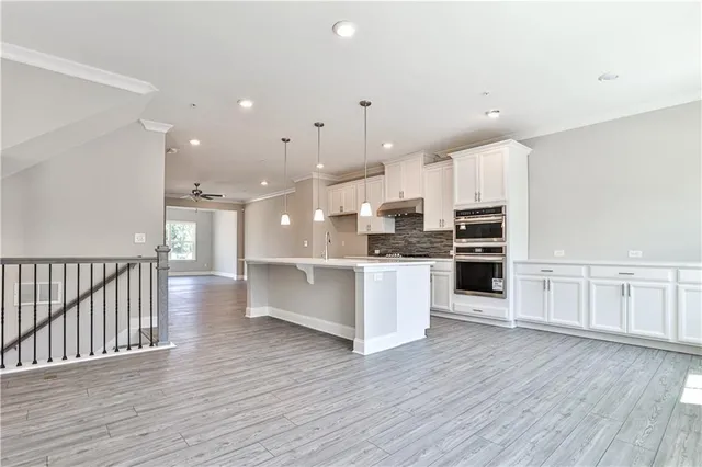 a large kitchen with stainless steel appliances kitchen island granite countertop a stove a refrigerator a sink and white cabinets with wooden floor