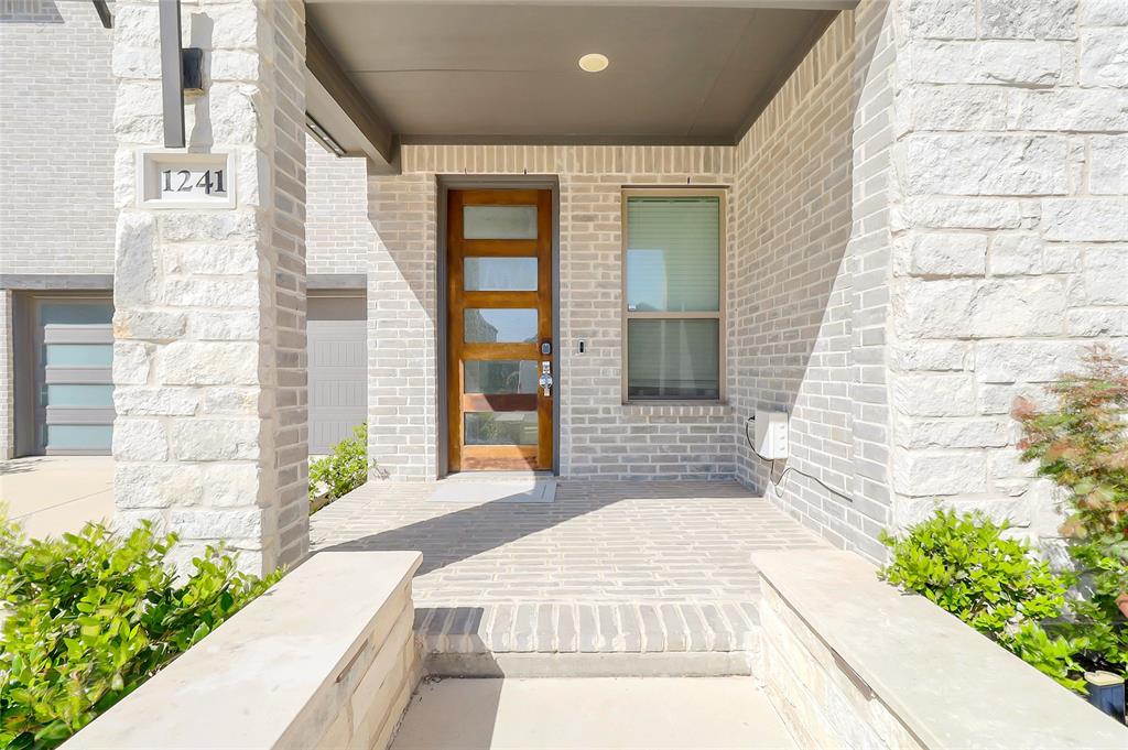 1241 Lupine Road Prosper, TX 75078 - Photo 2 of 38 Contemporary entryway featuring a rich wood-finish door with frosted glass panels, light-toned brick facade, stone-clad columns, and a covered porch with recessed lighting