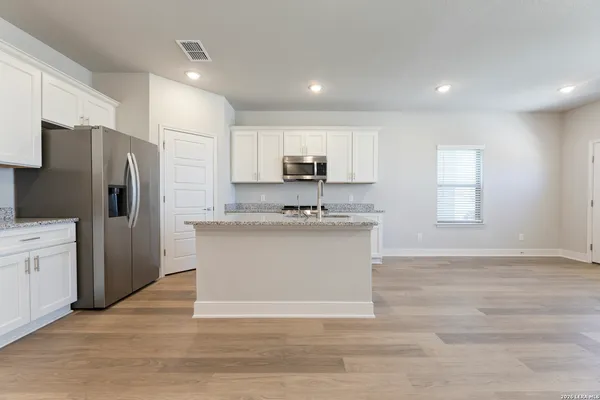 a view of kitchen with stainless steel appliances granite countertop a stove a sink a refrigerator and white cabinets with wooden floor